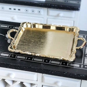 May include: A gold-coloured serving tray with two handles. The tray has a decorative, ornate border.