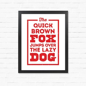 May include: A white framed print with a red distressed text design that reads "The quick brown fox jumps over the lazy dog."