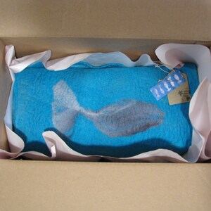 May include: A blue felt wall hanging with a white fish design. The hanging is packaged in a cardboard box with pink tissue paper.