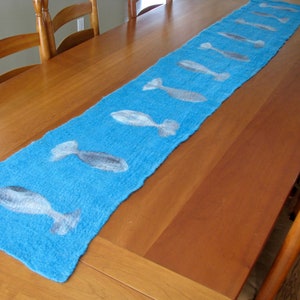 May include: A blue table runner with a white fish design. The runner is on a wooden table.