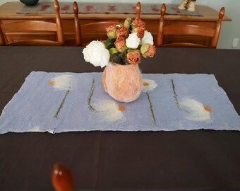 May include: A light blue felt table runner with white embroidered flowers and a vase of peach and white flowers in the center.
