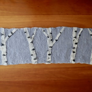 May include: A hand-felted wool wall hanging featuring a design of birch trees in white and black on a light blue background.