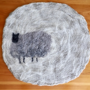 May include: A round, grey, felted rug with a black sheep design in the centre.