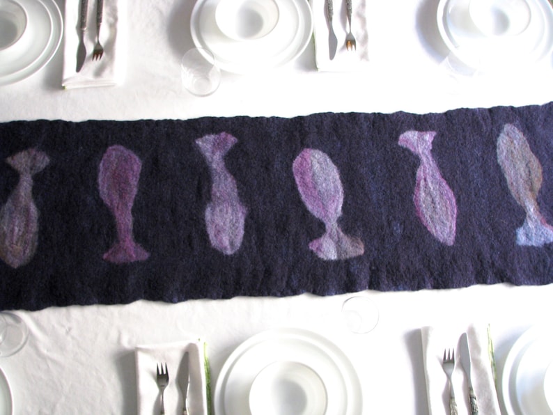 May include: A dark purple felt table runner with a repeating pattern of stylized fish silhouettes. The fish are a light purple color.