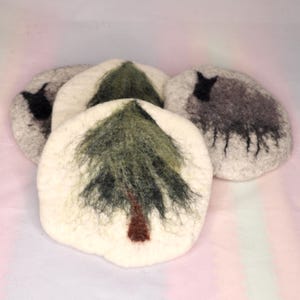 May include: Four felted wool coasters. Two coasters feature a green and brown tree design, while the other two have a grey sheep design. The coasters are round and have a textured appearance.
