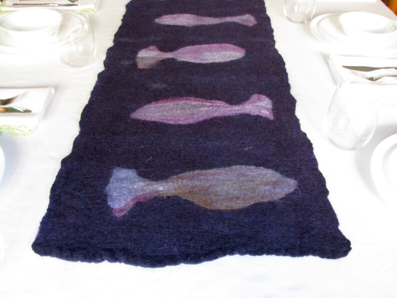 May include: A dark blue felt table runner with a design of five light purple and gray fish.