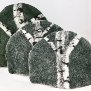 May include: Three green felt coasters with a white birch tree design. The coasters are round and have a fuzzy texture.