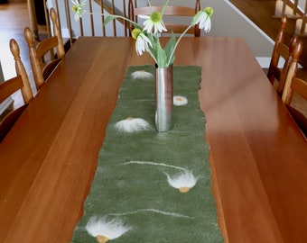 May include: A green felt table runner with white daisy designs. The runner is on a wooden table with a silver vase of white daisies.
