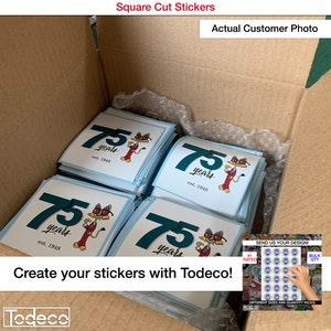 Puede incluir: Una caja llena de pegatinas cuadradas con un personaje de dibujos animados que lleva gafas de sol y el texto "75 a&ntilde;os est. 1948". Las pegatinas est&aacute;n impresas en papel blanco con fondo azul. La caja est&aacute; etiquetada como "Pegatinas cuadradas" y "Foto real de un cliente".