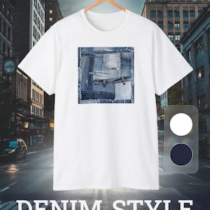 May include: A white short-sleeved t-shirt featuring a square graphic print on the chest composed of various shades of blue denim fabric patches with frayed edges. The shirt is displayed on a wooden hanger against a city street background.