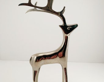 May include: Silver metal deer candle holder with a single candle cup on top of the antlers. The deer is standing on four legs.