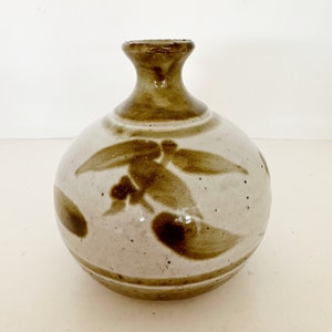 May include: A small, round, white ceramic vase with brown painted designs. The vase has a narrow neck and a wide base.