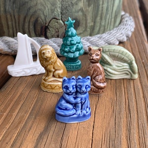 May include: A collection of six miniature ceramic figurines, including a sailboat, a lion, a Christmas tree, a cat, a leaf, and two cats hugging. The figurines are all hand-painted and feature intricate details.