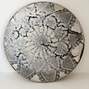 May include: A white ceramic plate with a black lace design. The plate has a rough, textured surface.