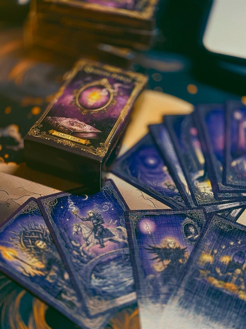 May include: A tarot deck featuring a dark purple box with gold ornate borders and the text Tarot Deck. Several cards are fanned out, displaying intricate illustrations of figures, horses, and glowing lanterns in shades of deep blue and purple.