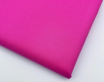 May include: A close-up shot of a vibrant fuchsia fabric. The material is folded, revealing a textured surface. The bright pink color dominates the image, creating a bold and eye-catching visual.