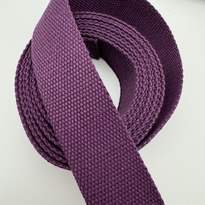 Puede incluir: Primer plano de un rollo de tela tejida morada. La tela es de color liso con una superficie texturizada. El material está tejido apretado y parece ser un textil resistente, adecuado para diversos proyectos de artesanía o costura.
