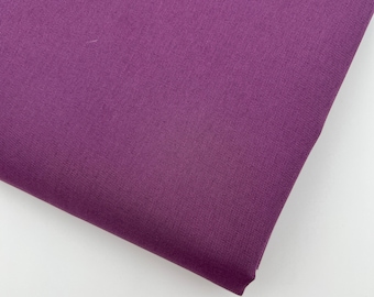 May include: A close-up of a folded piece of fabric in a deep purple hue. The fabric has a fine, textured weave, and the folds create shadows that highlight the material's depth and texture. The background is plain white.
