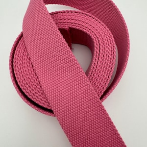 Peut inclure: Une bobine de sangle en coton rose, étroitement tissée et enroulée. La sangle est d'une couleur rose vif et unie, et la texture du tissage est clairement visible. Le matériau semble robuste et adapté à divers projets de couture.