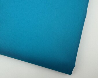 May include: A close-up shot of a folded piece of teal fabric. The fabric has a smooth texture and a slight sheen, with a visible diagonal weave pattern. The color is a vibrant, solid teal, with no other colors present.