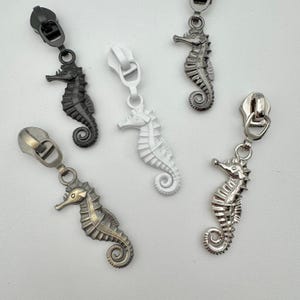 May include: Assortment of seahorse zipper pulls in various metallic finishes: black, white, bronze, and silver. These decorative zipper pulls are designed with detailed seahorse shapes, perfect for adding a unique touch to bags, clothing, or accessories.