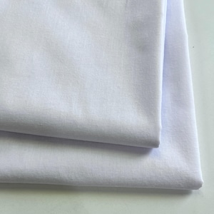 May include: Two folded white fabric pieces, likely linen or cotton, are layered. The fabric has a slightly textured surface, and the folds create shadows, enhancing the visual depth. The overall impression is of clean, crisp textiles.