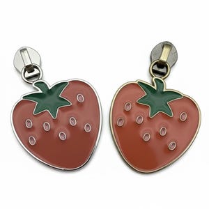 May include: Two strawberry-shaped zipper pulls. Each pull features a red enamel strawberry with a green stem and small white seeds. One has a silver-tone pull, the other a brass-tone pull.