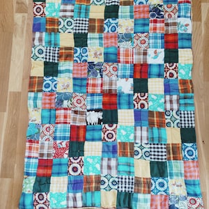 Può includere: Una trapunta patchwork con una varietà di quadrati di tessuto colorati. La trapunta presenta quadrati in tonalità di blu, verde, rosso, giallo e marrone, con disegni floreali, a quadri e fantasia. La trapunta è rettangolare e sembra fatta a mano.