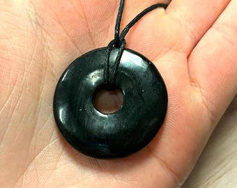 May include: Black obsidian donut pendant on a black cord necklace. The pendant is smooth and polished with a hole in the center.