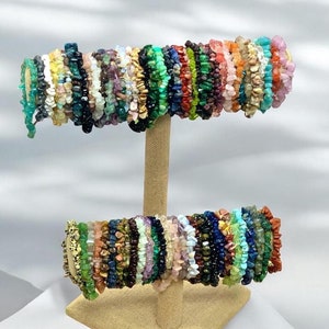 May include: A display of colorful gemstone chip bracelets on a wooden stand. The bracelets are made with various types of stones, including amethyst, turquoise, and jasper.