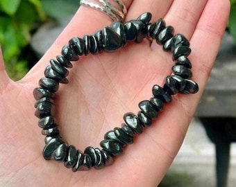May include: A black gemstone bracelet made of small, flat, irregularly shaped beads. The bracelet is made of natural black stones and is worn on a person's wrist.