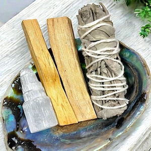 May include: A set of smudging tools including white sage, palo santo sticks, and a clear selenite crystal tower, all arranged in a iridescent abalone shell.