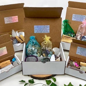 May include: Five open cardboard boxes with white interiors, each containing a variety of crystals, stones, and other items. The boxes are labeled with the contents, including "Ground OR Box", "White Crystal Trunk", "Amethyst Gem Box", "Pink Gem Box", and "Green Gem Box".