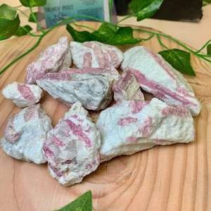 May include: A collection of raw pink tourmaline crystals with white and gray striations. The crystals are rough and have a natural, unpolished look.