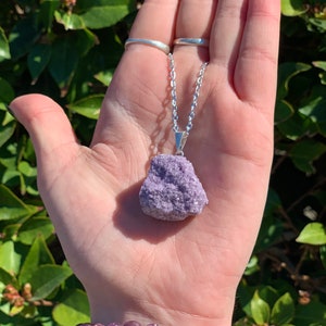 Op de afbeelding: Een zilveren ketting met een grote, ruwe, paarse lepidolietkristal hanger.