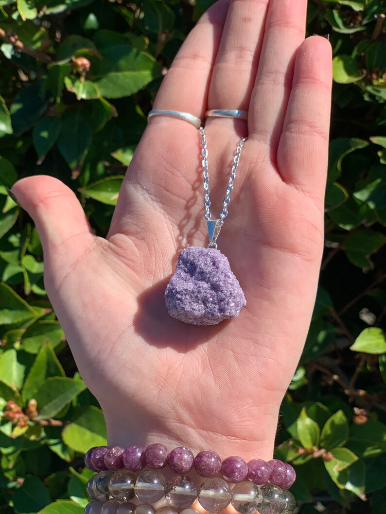 Op de afbeelding: Een zilveren ketting met een grote, ruwe, paarse lepidolietkristal hanger.