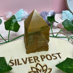 May include: A yellow and green natural stone pyramid point, also known as a crystal, on a wooden base with the text "SILVER POST" engraved on it.