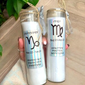 Puede incluir: Dos velas de vidrio blanco con etiquetas hologr&aacute;ficas que representan los signos del zod&iacute;aco Capricornio y Virgo. La vela de Capricornio tiene las fechas del 22 de diciembre al 19 de enero y las palabras "Responsable, Disciplinado, Ambicioso". La vela de Virgo tiene las fechas del 23 de agosto al 22 de septiembre y las palabras "Anal&iacute;tico, Pr&aacute;ctico, Meticuloso".