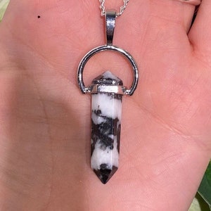 May include: A silver chain necklace with a black and white crystal pendant. The pendant is a point with a silver ring around the top.