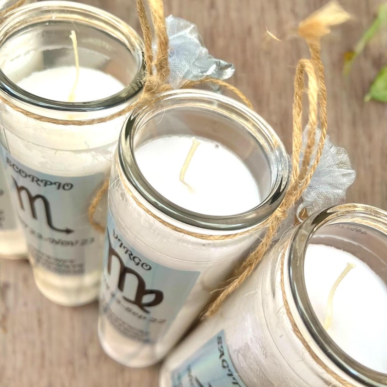 Puede incluir: Tres tarros de velas de vidrio con velas blancas y signos del zod&iacute;aco en las etiquetas. Los tarros est&aacute;n atados con cuerda y una cinta azul. Los signos del zod&iacute;aco son Escorpio, Virgo y Sagitario.