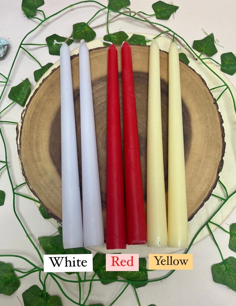 May include: Three pairs of taper candles in white, red, and yellow. The candles are arranged on a wooden surface.