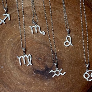 May include: A collection of silver necklaces with zodiac signs, each pendant is encrusted with small clear crystals.