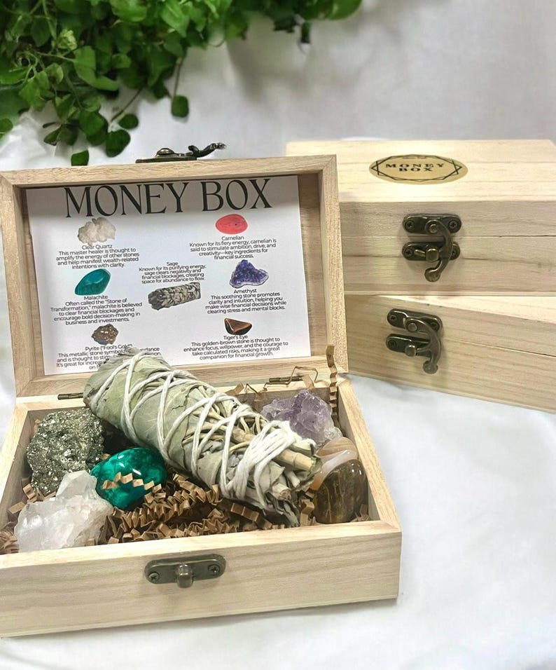 Peut inclure: Bo&icirc;te en bois avec un couvercle &agrave; charni&egrave;res, &eacute;tiquet&eacute;e "Money Box". La bo&icirc;te contient divers cristaux et un fagot de sauge, notamment du quartz clair, de la cornaline, de la malachite, de l'am&eacute;thyste, de l'&oelig;il de tigre et de la pyrite. La bo&icirc;te comprend &eacute;galement une carte avec des descriptions de chaque cristal et de ses propri&eacute;t&eacute;s.