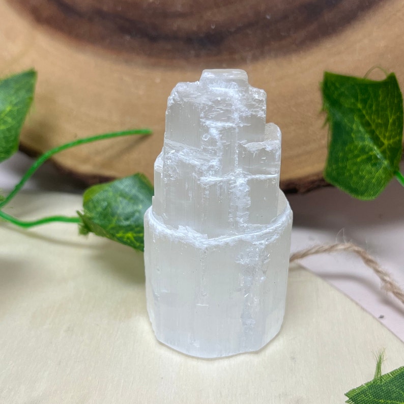 May include: A white selenite crystal tower with a layered, stacked design. The crystal is smooth and polished, with a translucent appearance.