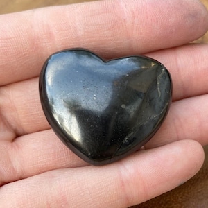 May include: A polished black heart-shaped stone. The stone is smooth and has a glossy finish.