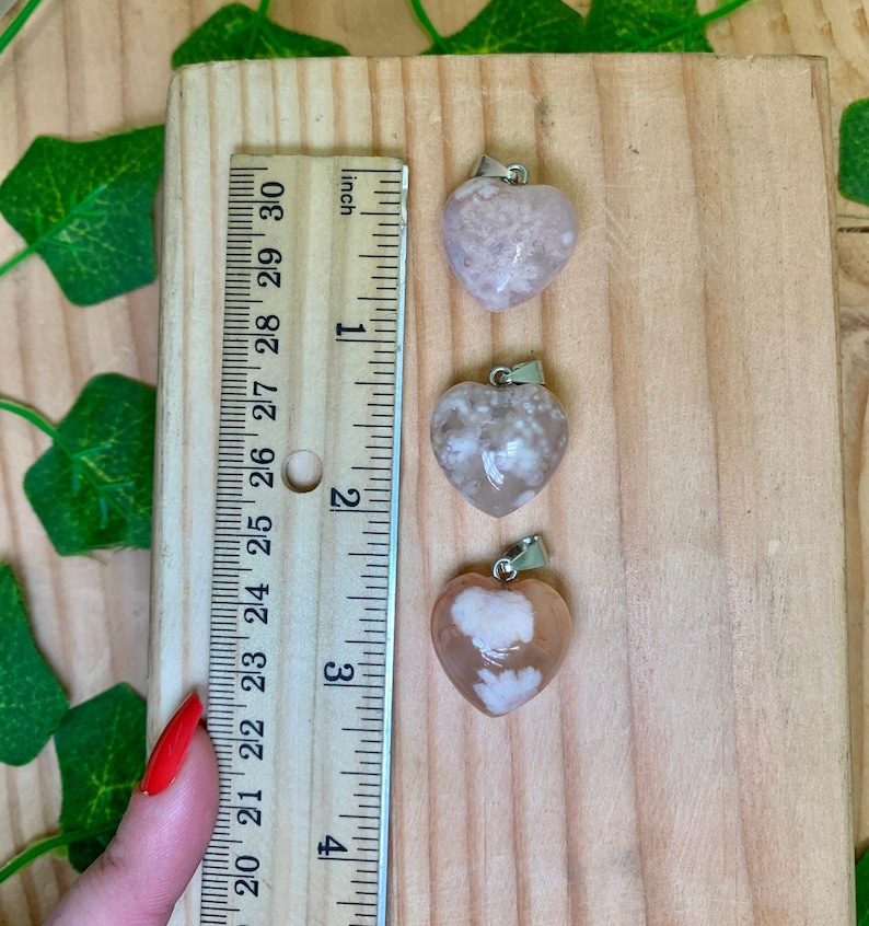 Puede incluir: Tres colgantes de coraz&oacute;n de &aacute;gata rosa con un aro de plata, medidos con una regla en pulgadas. Los colgantes miden aproximadamente 1 pulgada.