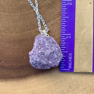 Op de afbeelding: Een zilveren ketting met een grote, ruwe, paarse lepidolietkristal hanger. De hanger is ongeveer 2,5 cm groot.