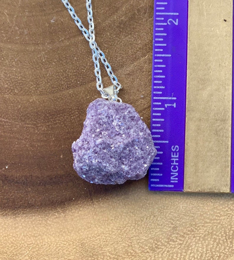 Op de afbeelding: Een zilveren ketting met een grote, ruwe, paarse lepidolietkristal hanger. De hanger is ongeveer 2,5 cm groot.