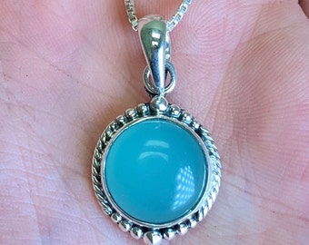 May include: A silver necklace with a round pendant featuring a light blue gemstone surrounded by a silver beaded border.