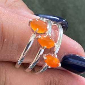 May include: A silver ring with three orange carnelian stones set in a criss-cross pattern.